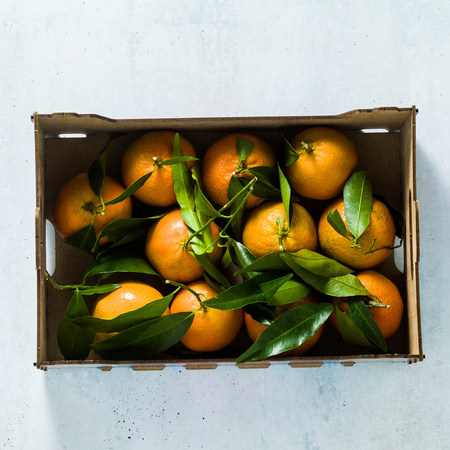 Fresh mandarin oranges fruit or tangerines with leaves in wooden box, top viewの写真素材