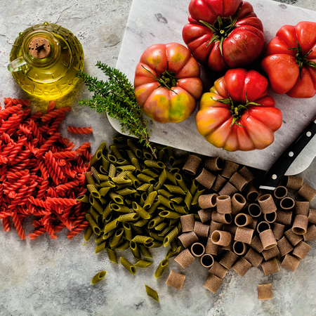 multicolor gluten-free pasta with ingredients from which it is made on a stone table with brandywine tomato and olive oilの写真素材