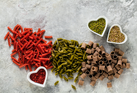 multicolor gluten-free pasta with ingredients in bowls in the form of hearts from which it is made on a stone tableの写真素材