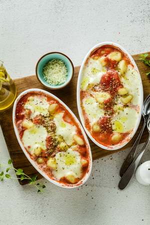Italian potato dumplings gnocchi alla sorrentina with mozzarella cheese, baked in the oven with tomato sauce and herbs. Served with parmesan and spices on the white kitchen table. Classic healthy vegetarian cuisineの写真素材