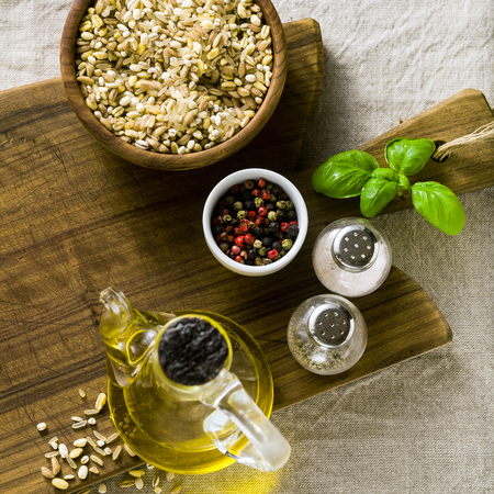 mix of cereals in a wooden bowl on a cutting board with olive oil, multicolored peppers and spices. food background home cooking on linen tableclothの写真素材