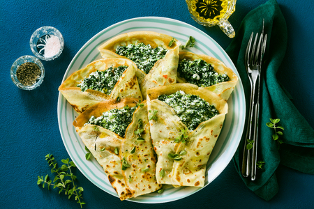 Traditional Italian pancakes crepes with spinach and ricotta on a served blue table. healthy vegetarian dietの写真素材