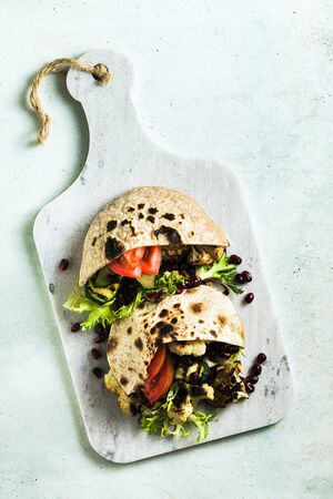 vegan pita with vegetables on a marble cutting board on a tableの写真素材