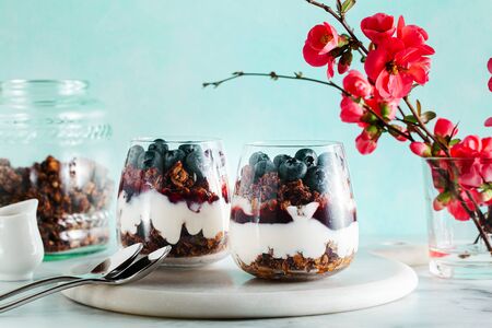 morning dessert with granola in a glass with yogurt, jam and fresh berries. spring branches of a blossoming tree. healthy breakfastの写真素材