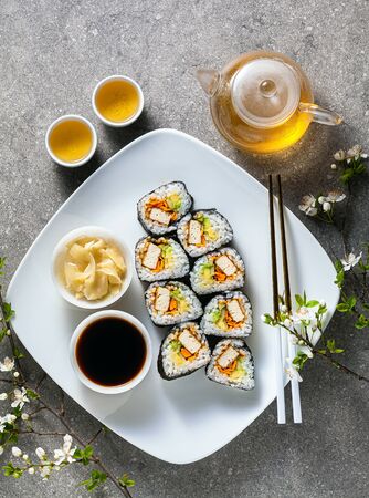 vegan sushi with tofu in General Tso sauce, avocado and fresh vegetables . on a table with branches of a blossoming tree and green tea in a glass teapotの写真素材