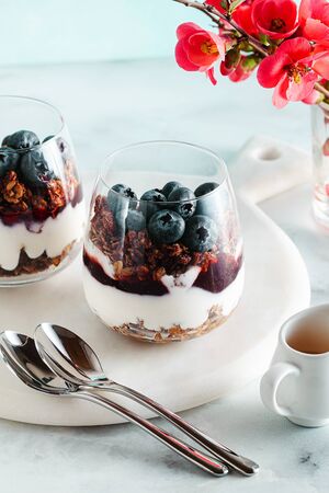 morning dessert with granola in a glass with yogurt, jam and fresh berries. spring branches of a blossoming tree. healthy breakfastの写真素材