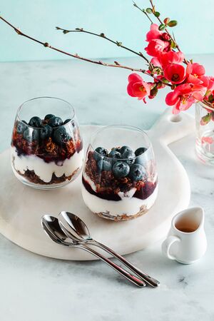morning dessert with granola in a glass with yogurt, jam and fresh berries. spring branches of a blossoming tree. healthy breakfastの写真素材