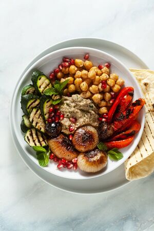 Italian Mediterranean Buddha bowl with Baba ghanoush caramelized onions, spicy chickpeas and grilled vegetables. healthy vegan food and pita breadの写真素材