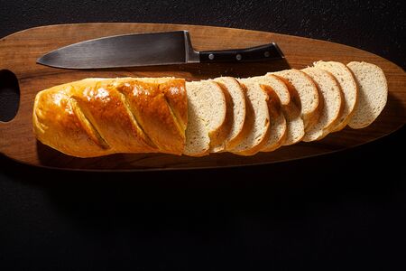 sliced loaf of bread on a chopping board and a chef's knife on a black backgroundの写真素材