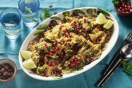 couscous is cooked on orange juice with boiled vegetables, caramelized onions, raisins and pomegranate seeds. on the table with a linen tableclothの写真素材