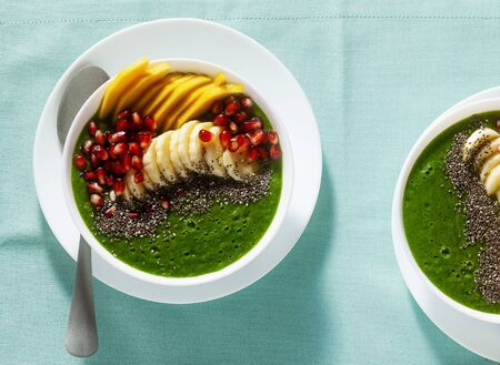 bowl of green smoothie with sliced mango, banana, pomegranate seeds and chia seeds, maple syrup for a healthy morning breakfastの写真素材