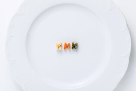 word MMM from dry multi-colored pasta on a white plate.の写真素材