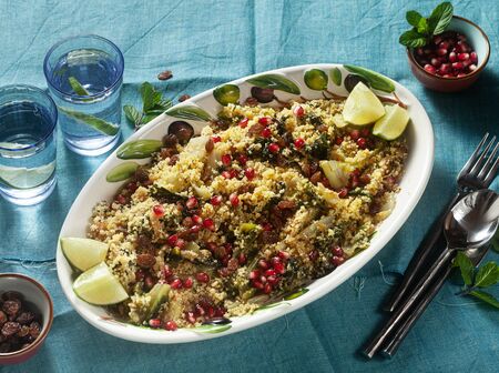 couscous is cooked on orange juice with boiled vegetables, caramelized onions, raisins and pomegranate seeds. on the table with a linen tableclothの写真素材