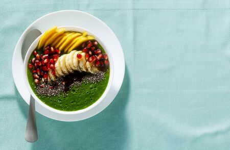 bowl of green smoothie with sliced mango, banana, pomegranate seeds and chia seeds, maple syrup for a healthy morning breakfastの写真素材
