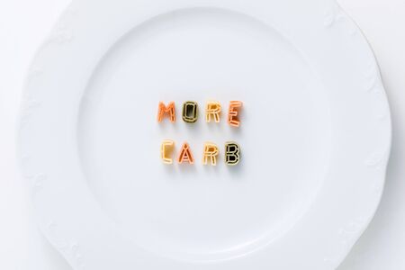 words MORE CARB from dry multi-colored pasta on a white plate.の写真素材