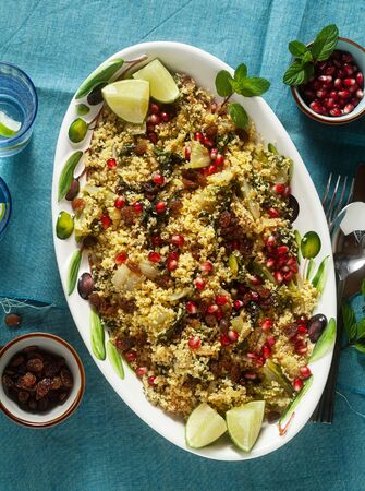 couscous is cooked on orange juice with boiled vegetables, caramelized onions, raisins and pomegranate seeds. on the table with a linen tableclothの写真素材
