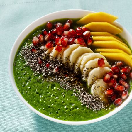 bowl of green smoothie with sliced mango, banana, pomegranate seeds and chia seeds, maple syrup for a healthy morning breakfastの写真素材