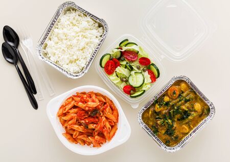 takeaway food in disposable containers: rice, vegetable curry, Italian pasta with tomato sauce and fresh healthy salad.の写真素材