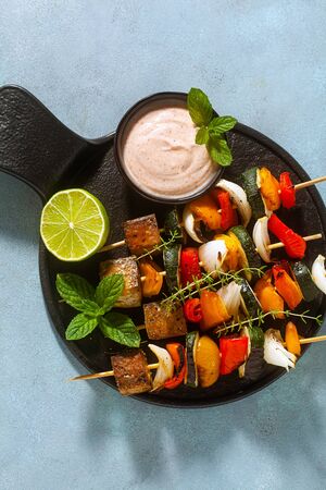ready vegan kebabs of vegetables and smoked tofu with cashew sauce and smoked paprika on a blue backgroundの写真素材