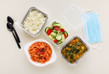 takeaway food in disposable containers: rice, vegetable curry, Italian pasta with tomato sauce and fresh healthy salad. and medical mask. quarantineの写真素材