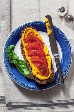 a sandwich with baked pumpkin hummus and tomatoes on a plate and a linen tablecloth. healthy snackの写真素材