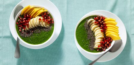 banner of bowl of green smoothie with sliced mango, banana, pomegranate seeds and chia seeds, maple syrup for a healthy morning breakfastの写真素材