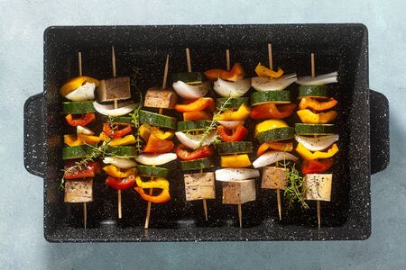 vegan kebabs of vegetables and smoked tofu, in a baking sheet, ready for baking in the oven on a blue backgroundの写真素材