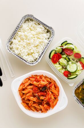 takeaway food in disposable containers: rice, vegetable curry, Italian pasta with tomato sauce and fresh healthy salad.の写真素材