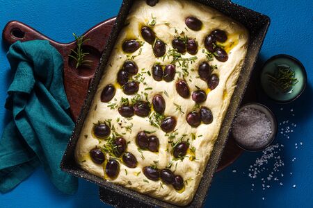 uncooked focaccia with red grapes on a blue table in a baking sheet. ready for baking. Italian Cuisineの写真素材