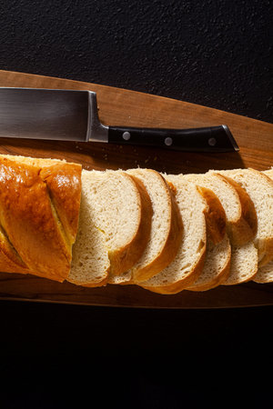 sliced loaf of bread on a chopping board and a chef's knife on a black background