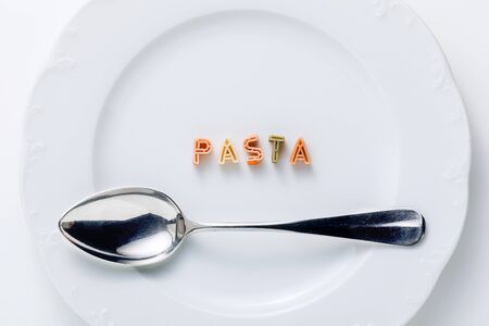 word PASTA from dry multi-colored pasta on a white plate and spoonの写真素材