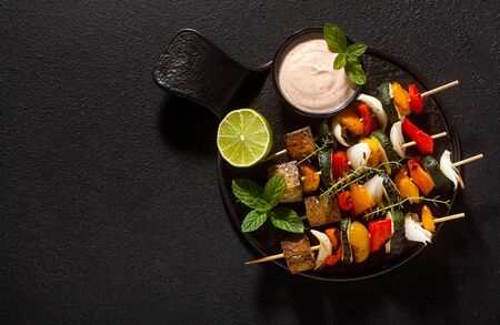 ready vegan kebabs of vegetables and smoked tofu with cashew sauce and smoked paprika on a black backgroundの写真素材