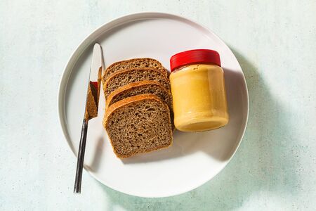 peanut butter in a jar and whole grain bread with a knife on the table.の写真素材