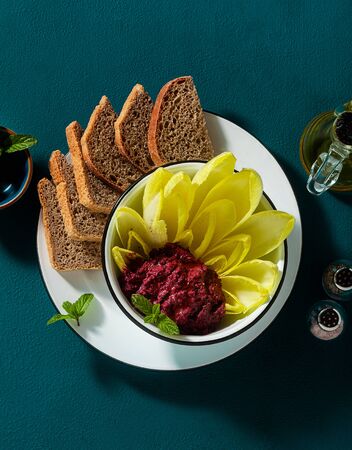 vegan snack of spread of roasted beets and pistachios and leaves of Belgian Endive with whole grain bread on the tableの写真素材