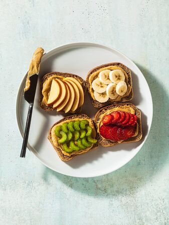 various sandwiches with peanut butter and strawberries, celery, banana and apple on a plate on the table. perfect morning breakfastの写真素材