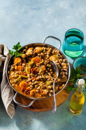 Black-eyed Pea Vegan Chili in a metal pan on a wooden stand on a blue backgroundの写真素材
