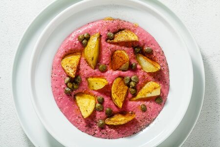 summer dish with pink hummus from cannellini beans and beets with fried potatoes and capers in a plate on the tableの写真素材