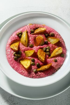 summer dish with pink hummus from cannellini beans and beets with fried potatoes and capers in a plate on the tableの写真素材