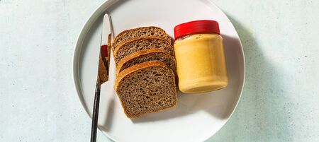 banner of peanut butter in a jar and whole grain bread with a knife on the table.の写真素材