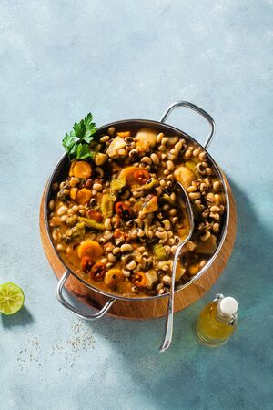 Black-eyed Pea Vegan Chili in a metal pan on a wooden stand on a blue backgroundの写真素材