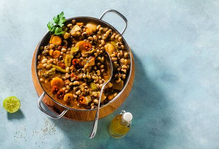 Black-eyed Pea Vegan Chili in a metal pan on a wooden stand on a blue backgroundの写真素材