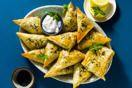 indian samosa made with phyllo with spicy potatoes and vegetables , served with yogurt, mint and lemon on a blue backgroundの写真素材