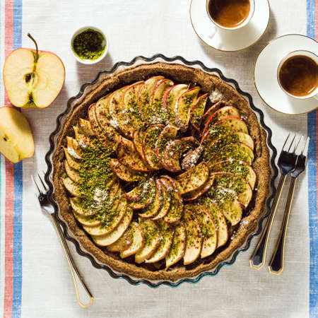italian apple pie crostata with pistachio crumbs on the table with a white tablecloth and cups of coffee espressoの写真素材