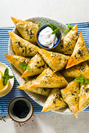 indian samosa made with phyllo with spicy potatoes and vegetables , served with yogurt, mint and lemon on a blue napkin in a restaurantの写真素材