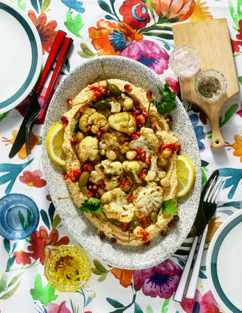 hummus with baked cauliflower and pomegranate seeds on a table with a bright colorful tableclothの写真素材