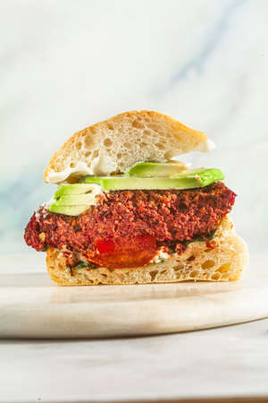 cut vegan burger without meat with avocado, tomatoes and spinach on the table and red wine in a glassの写真素材