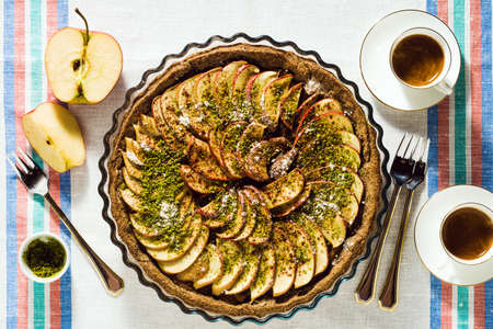 italian apple pie crostata with pistachio crumbs on the table with a white tablecloth and cups of coffee espressoの写真素材