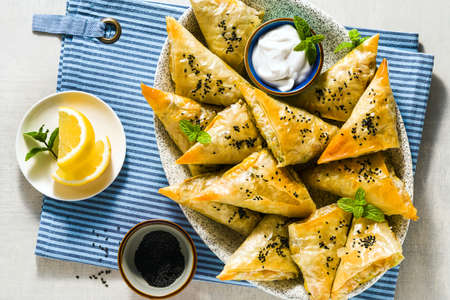indian samosa made with phyllo with spicy potatoes and vegetables , served with yogurt, mint and lemon on a blue napkin in a restaurantの写真素材