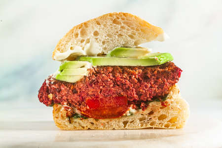 cut vegan burger without meat with avocado, tomatoes and spinach on the table and red wine in a glassの写真素材