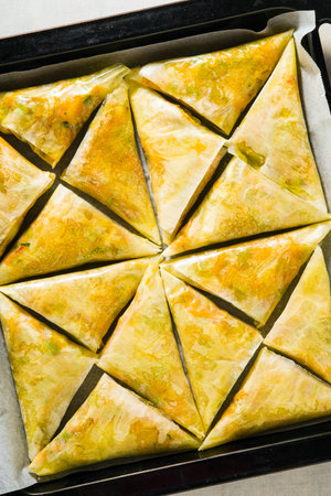 indian samosa made with phyllo with spicy potatoes and vegetables on a baking sheet, ready to be...